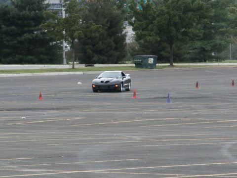 2001 Mercury Grand Marquis - A black Pontiac Firebird navigates a course marked by traffic cones in an empty parking lot.