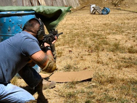 1990 Ford Bronco - A shooter takes aim at a target range, with a blue barrel and distant targets visible.