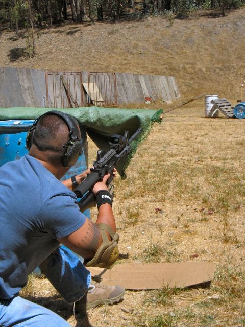 1990 Ford Bronco - A person kneels and aims a rifle at a target range, wearing headphones and protective gear.