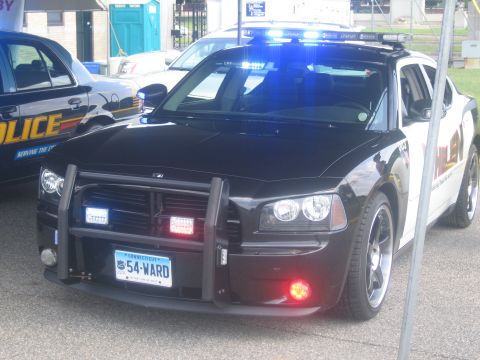 1991 Ford LTD Crown Victoria - black Dodge Charger police car with front push bar and lit blue lights, Connecticut plate 54-WARD, parked under a tent.