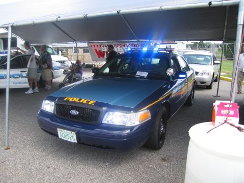 1991 Ford LTD Crown Victoria - dark blue Ford Crown Victoria POLICE car with its blue lightbar flashing, parked under a tent with people nearby.