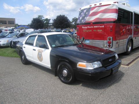 1991 Ford LTD Crown Victoria - black-and-white Ford Crown Victoria police car parked on pavement beside a red bus painted with an American flag.