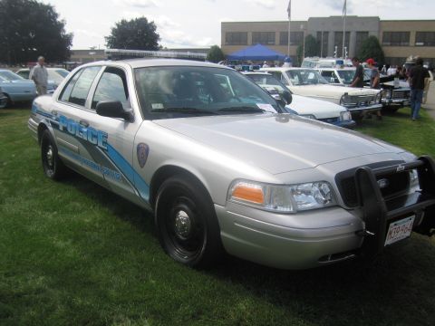 1991 Ford LTD Crown Victoria - silver and blue Ford police cruiser lettered "Police" with a front push bar, displayed on grass among other cars.