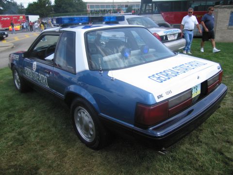 1991 Ford LTD Crown Victoria - Rear of a blue-and-white Ford Mustang marked "Georgia State Patrol" with light bar, displayed on grass as people walk past.