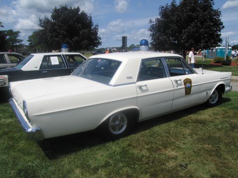 1991 Ford LTD Crown Victoria - white vintage Ford four-door sedan with a single blue dome light and police door shield, parked on grass.