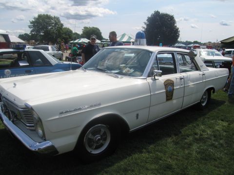 1991 Ford LTD Crown Victoria - white vintage Ford Galaxie four-door sedan with blue dome light and police door shield, parked on grass at a show.