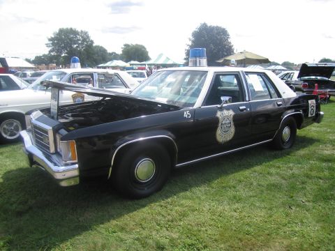 1991 Ford LTD Crown Victoria - black-and-white full-size Ford police sedan numbered 45 with hood open, police shield on the door, parked on grass.