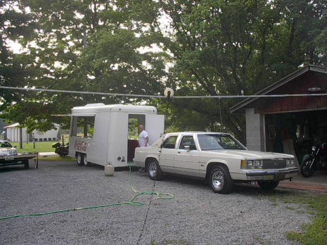 White 1980s Ford sedan parked next to a Coca-Cola trailer
