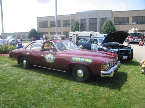 1991 Ford LTD Crown Victoria - maroon 1970s Pontiac two-door lettered "State Patrol" with roof light bar and Missouri patrol shield, parked on grass.