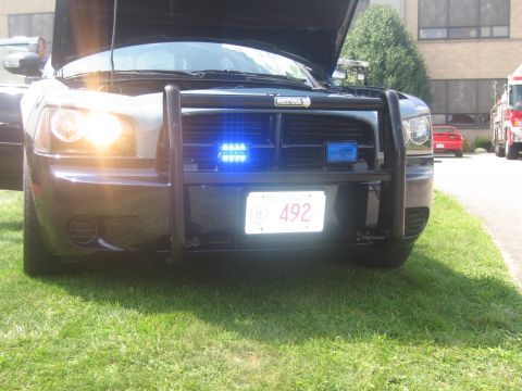 1991 Ford LTD Crown Victoria - Front of a black Dodge Charger police car with push bar and lit blue strobe lights, plate 492, hood open.