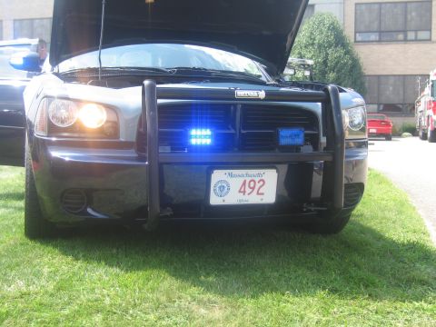 1991 Ford LTD Crown Victoria - Front of a black Dodge Charger police car with push bar, lit blue strobes, hood open and a Massachusetts plate 492.