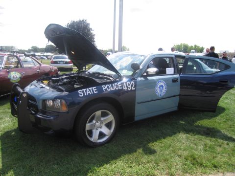 1991 Ford LTD Crown Victoria - two-tone Dodge Charger lettered "State Police 492" with Massachusetts shield, hood and door open, parked on grass.