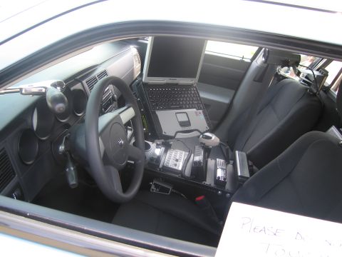 1991 Ford LTD Crown Victoria - Interior of a police car showing a mounted laptop, radio console between the seats, and a handwritten "please do not touch" sign.