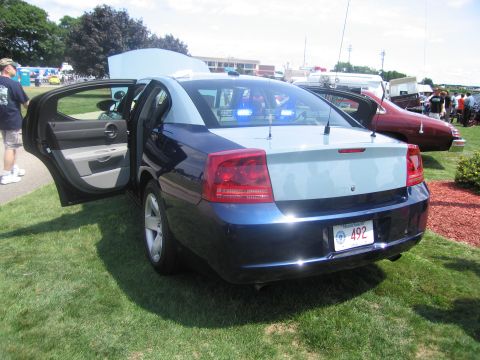 1991 Ford LTD Crown Victoria - Rear three-quarter view of a dark blue Dodge Charger police sedan with rear doors open and a Massachusetts plate reading 492 on grass.