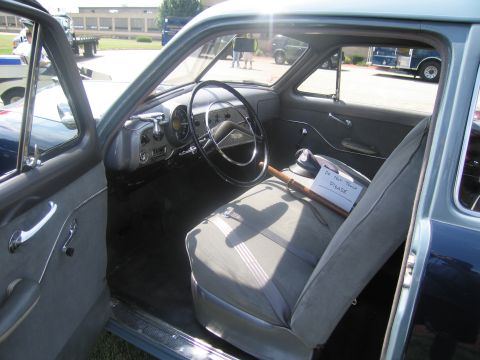 1991 Ford LTD Crown Victoria - Interior of a vintage sedan showing a gray cloth bench seat, large steering wheel, and a small paper sign on the seat.