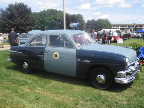1991 Ford LTD Crown Victoria - Driver-side view of a restored two-tone blue vintage Ford four-door police sedan with roof spotlight and agency door seal at a car show.