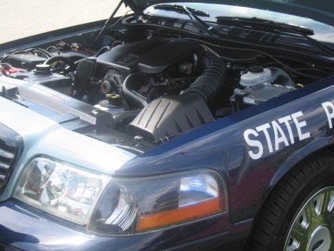 1991 Ford LTD Crown Victoria - Open engine bay of a dark blue State Police car with the hood raised, the fender lettered STATE P, beside the front headlight.