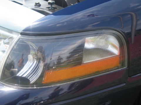 1991 Ford LTD Crown Victoria - Close-up of the front headlight assembly and amber turn-signal lens on a dark blue vehicle with reflections in the glass.