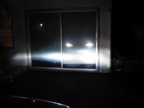 1995 Ford Thunderbird - Bright headlights illuminate a dark scene, reflecting off a glass door. The Supermotors.net logo is visible in the corner.