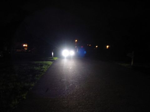 1995 Ford Thunderbird - Headlights shine brightly on a dark, wet road, with a blue lens flare distorting the view.