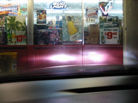 1995 Ford Thunderbird - Headlights from a car shine on a store window filled with various beer advertisements.