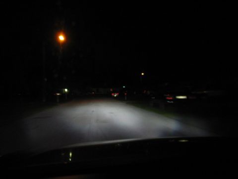 1995 Ford Thunderbird - Headlights illuminate a dark street from the perspective of the driver's seat, with other vehicles visible in the distance.