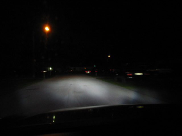Dashboard view of headlights illuminating a dark street at night