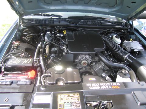 1991 Ford LTD Crown Victoria - Close engine-bay view of a police car showing the black V8 engine and a sticker joking that the next police car will have a Hemi.
