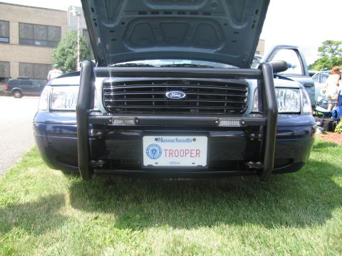 1991 Ford LTD Crown Victoria - Front view of a dark blue Ford police car with a black push bumper and a Massachusetts plate reading TROOPER under the raised hood.