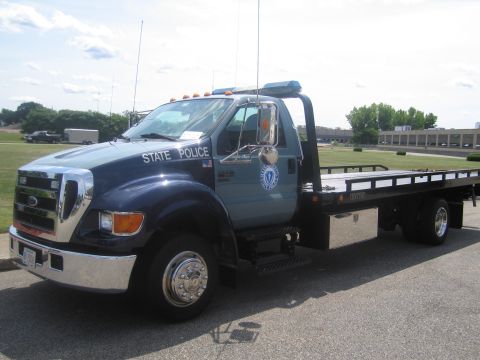 1991 Ford LTD Crown Victoria - Driver-side view of a two-tone blue Ford State Police flatbed tow truck with an empty bed and agency seal on the door.