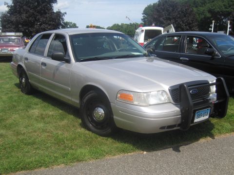 1991 Ford LTD Crown Victoria - Front three-quarter view of a silver Ford Crown Victoria police interceptor with a black push bumper and steel wheels parked on grass.