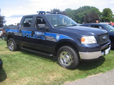 1991 Ford LTD Crown Victoria - Side view of a dark blue Ford F-150 crew-cab pickup lettered UMASS POLICE with light bar and graphics, parked on grass.