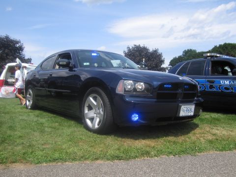 1991 Ford LTD Crown Victoria - Front three-quarter view of a dark blue Dodge Charger police sedan with activated blue grille lights, beside a UMass Police car.