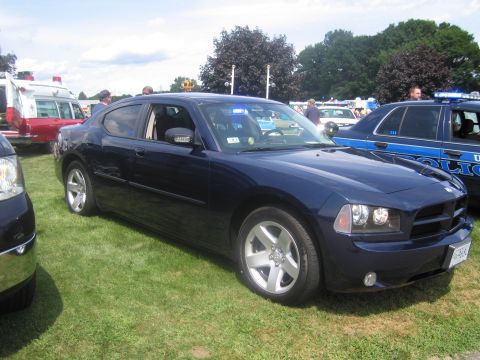 1991 Ford LTD Crown Victoria - Driver-side front three-quarter view of a dark blue Dodge Charger police sedan parked on grass among other vehicles at a car show.