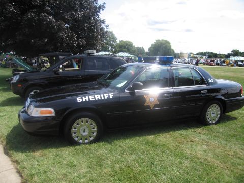 1991 Ford LTD Crown Victoria - black Ford Crown Victoria sheriff's patrol sedan marked SHERIFF with a gold star decal, parked on grass at an outdoor show.