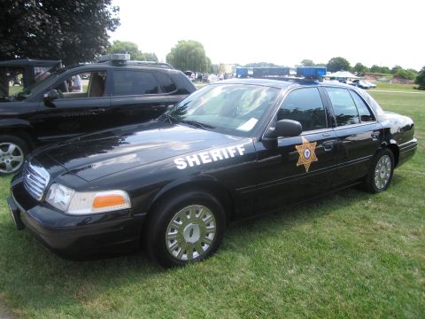 1991 Ford LTD Crown Victoria - black Ford Crown Victoria sheriff's sedan marked SHERIFF with a gold star, photographed front-three-quarter on grass at a show.