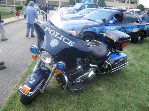1991 Ford LTD Crown Victoria - dark blue police touring motorcycle marked POLICE with number 2 and emergency lights, parked beside a UMass Police cruiser on grass.