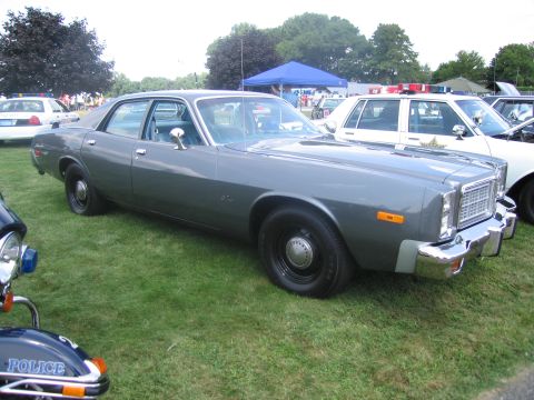 1991 Ford LTD Crown Victoria - two-tone gray 1970s full-size four-door sedan on grass, with a POLICE motorcycle in the foreground and cruisers behind.