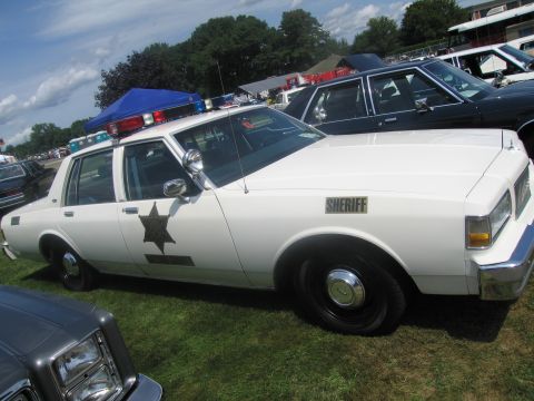 1991 Ford LTD Crown Victoria - Side view of a white boxy Chevrolet Caprice sheriff's sedan with star decal, SHERIFF lettering and a roof light bar, on grass.