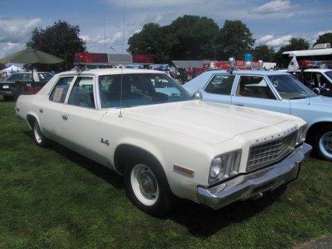 1991 Ford LTD Crown Victoria - white Plymouth Fury full-size four-door police sedan with light bar, parked on grass among other classic cruisers.