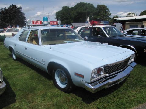 1991 Ford LTD Crown Victoria - light blue Plymouth Fury full-size four-door sedan parked on grass below a STATE POLICE sign, with other cruisers nearby.