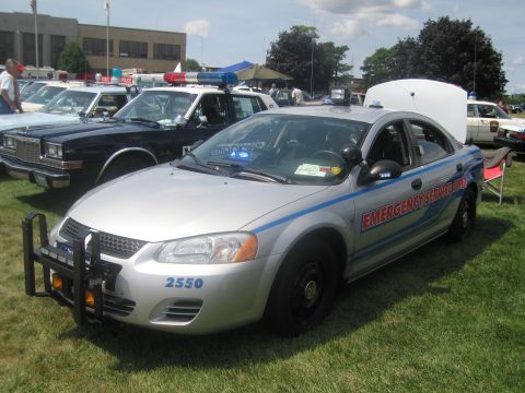 1991 Ford LTD Crown Victoria - silver Emergency Service Unit sedan numbered 2550, with a black push bar and red-blue striping, parked among police cars on grass.