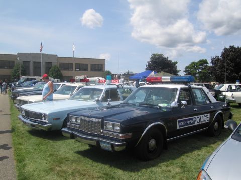 1991 Ford LTD Crown Victoria - line of vintage police sedans sits on a grassy field, led by a black-and-white North Haven Police cruiser, with a flag and building behind.