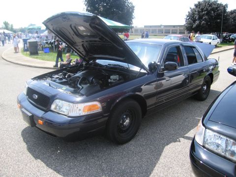 1991 Ford LTD Crown Victoria - dark Ford Crown Victoria police interceptor sits on pavement with its hood raised, exposing the engine bay at a car show.