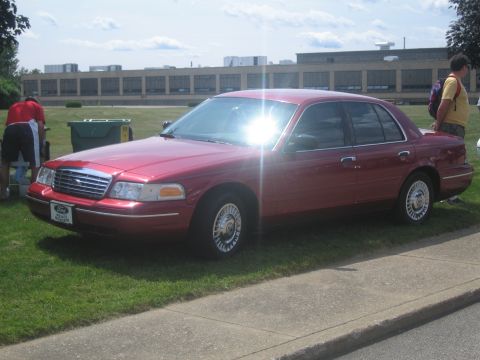 1991 Ford LTD Crown Victoria - red Ford Crown Victoria four-door sedan with chrome wheel covers is parked at a curb on a bright sunny day.