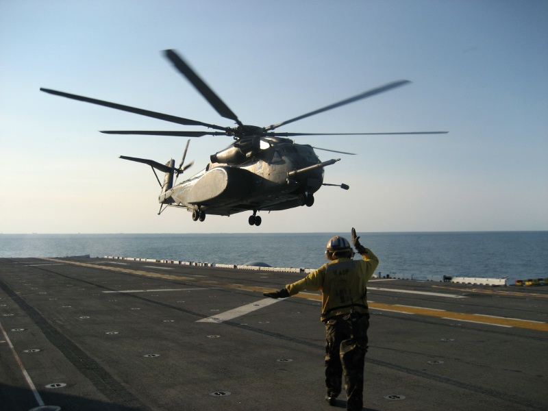 Helicopter hovering over deck with a yellow-shirted director below