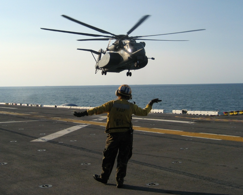 Helicopter hovering as a yellow-shirted director signals from the deck