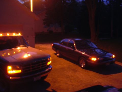 1996 Ford Crown Victoria - Two vehicles are parked outside a building at night, illuminated by artificial lights.