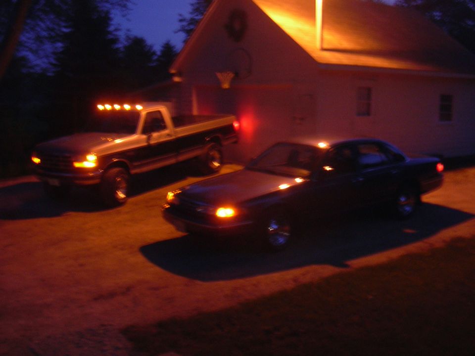 Dark sedan parked in front of a house at night, with a pickup truck behind it