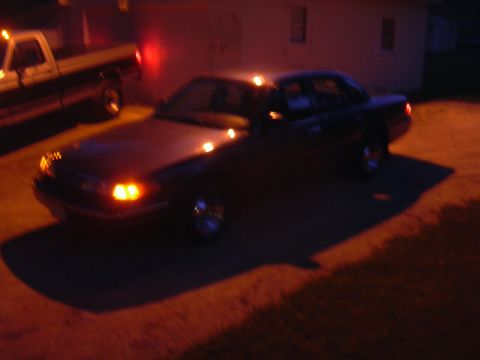 1996 Ford Crown Victoria - A dark sedan is parked next to a pickup truck under artificial light at night.